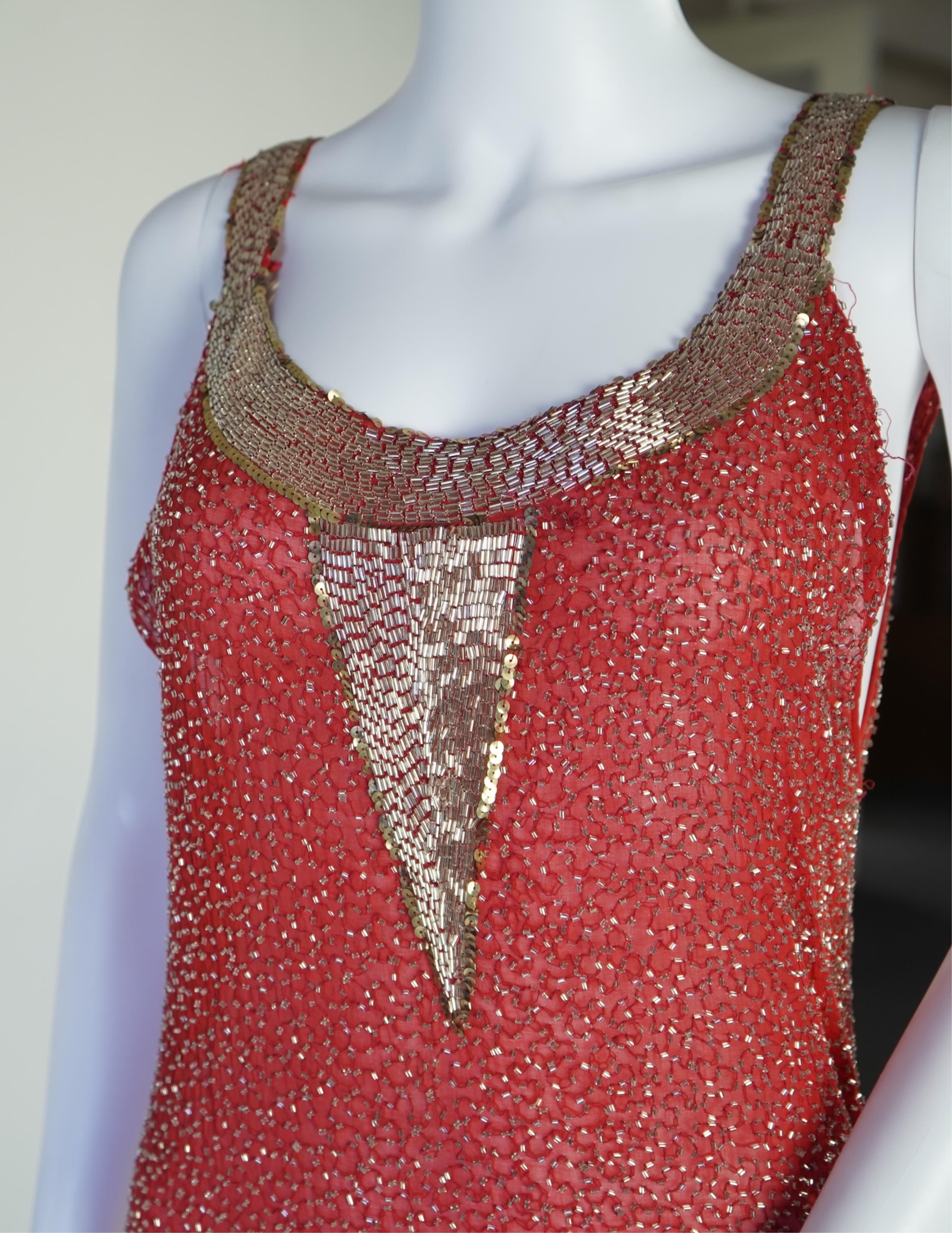 A 1920's red georgette beaded evening dress. Hand beaded and sequinned in white and gold, designed with a dropped waist, handkerchief points and wide beaded border with large stylistic floral motifs. Length 115cm. Condit